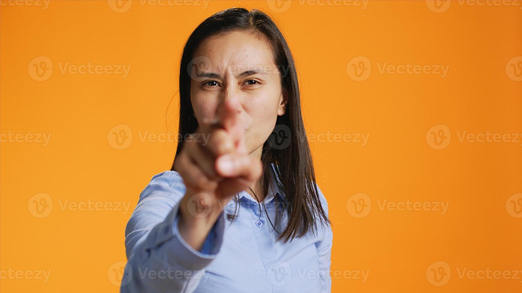 During the shot, pleased filipino girl points index finger at the lens. Confident young woman with calm mood using charm and personality, standing over orange background illustrating stuff. photo