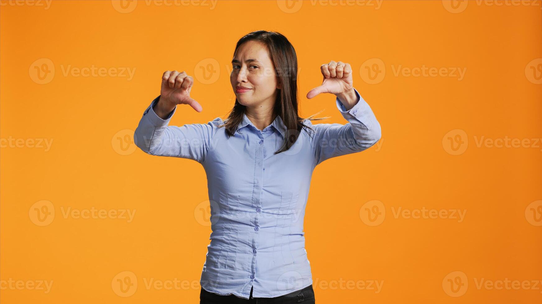 Asian person giving thumbs down in front of studio camera, expressing negativity and disapproval with dislike symbol. Negative woman showing rejection, being upset and displeased. photo