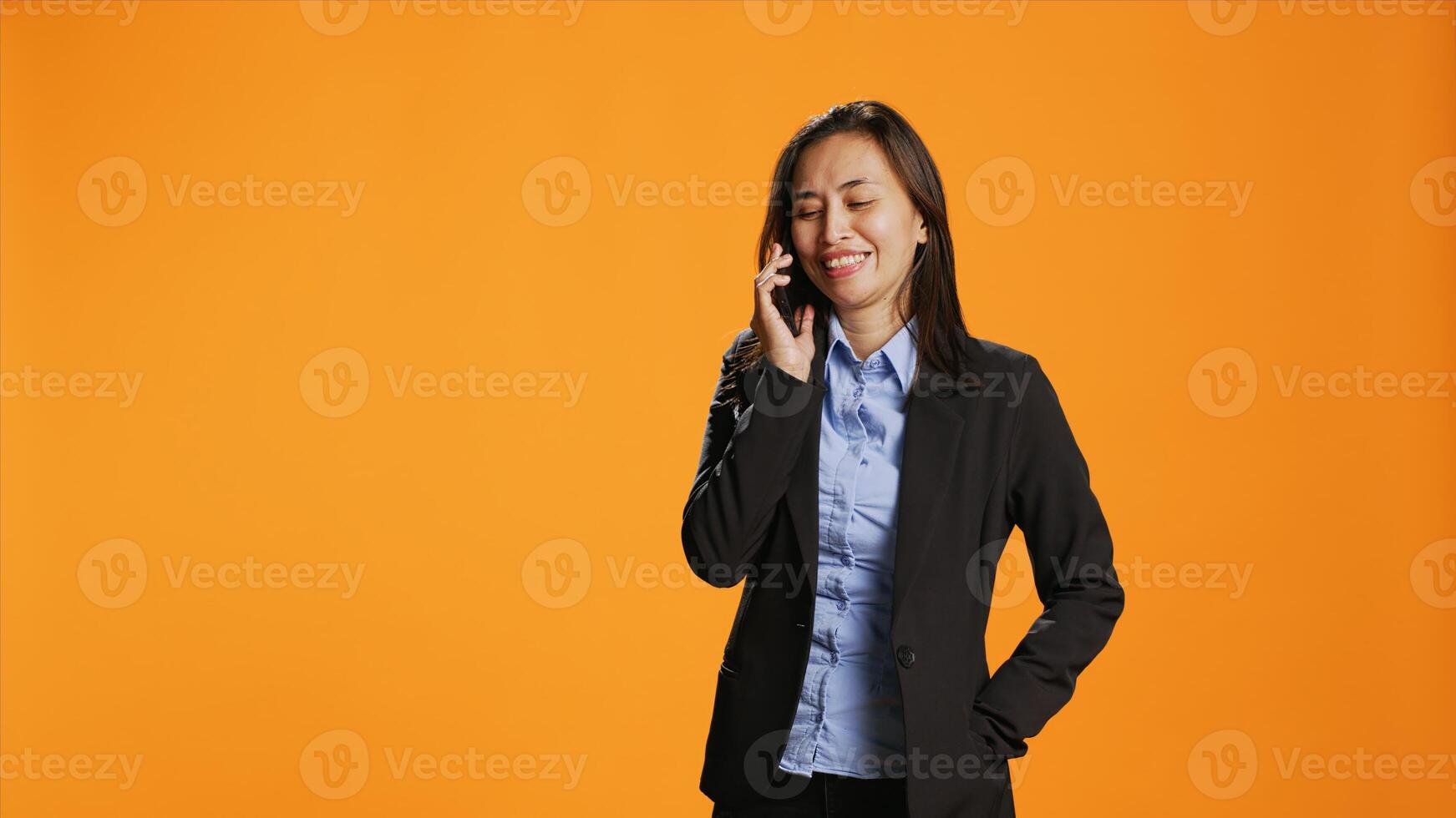 mujer de negocios utilizando teléfono inteligente a tomar remoto llamada en estudio, respondiendo móvil teléfono y hablando en frente de cámara. hembra modelo con chaqueta teniendo conversacion con jefe en dispositivo. foto