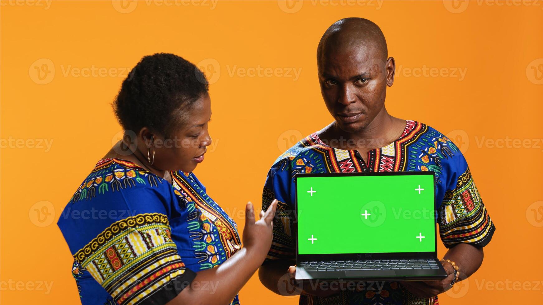 Ethnic couple pointing at laptop with greenscreen display, posing in studio with portable pc presenting isolated copyspace layout. Man and woman looking at blank mockup template on camera. photo