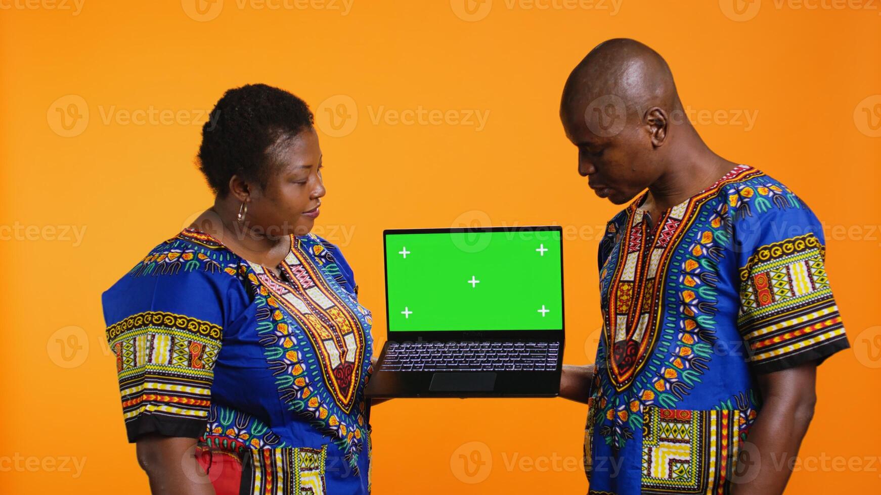 Ethnic people presenting laptop with greenscreen layout, showing blank mockup chromakey display and posing in studio. African american husband and wife pointing at isolated copyspace. photo