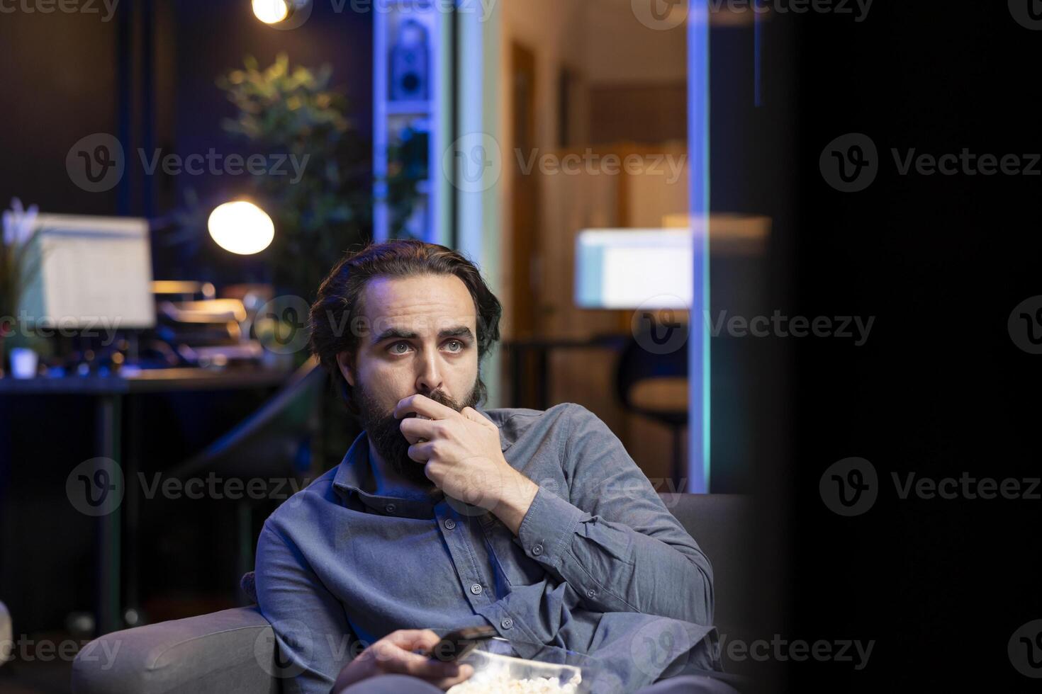 Sad man on couch eating popcorn from stress while watching heartbreaking drama movie on streaming service. Person consuming snack, distressed by TV show favorite character dies photo