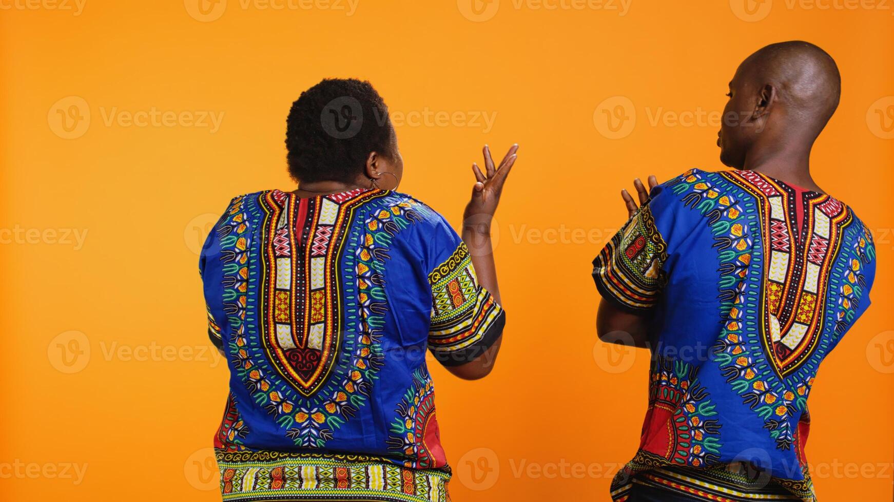 Back view of couple being sick and tired of arguing, man interrupting woman from yelling. African american people frustrated about having argument in studio, orange background. photo