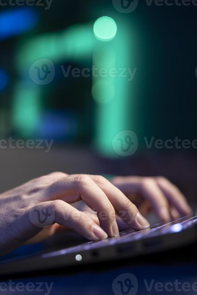 Close up shot of laptop used by freelancer working from home in RGB lit apartment typing on keyboard. Focus on notebook used by teleworking accountant writing audit on couch in blurry background photo