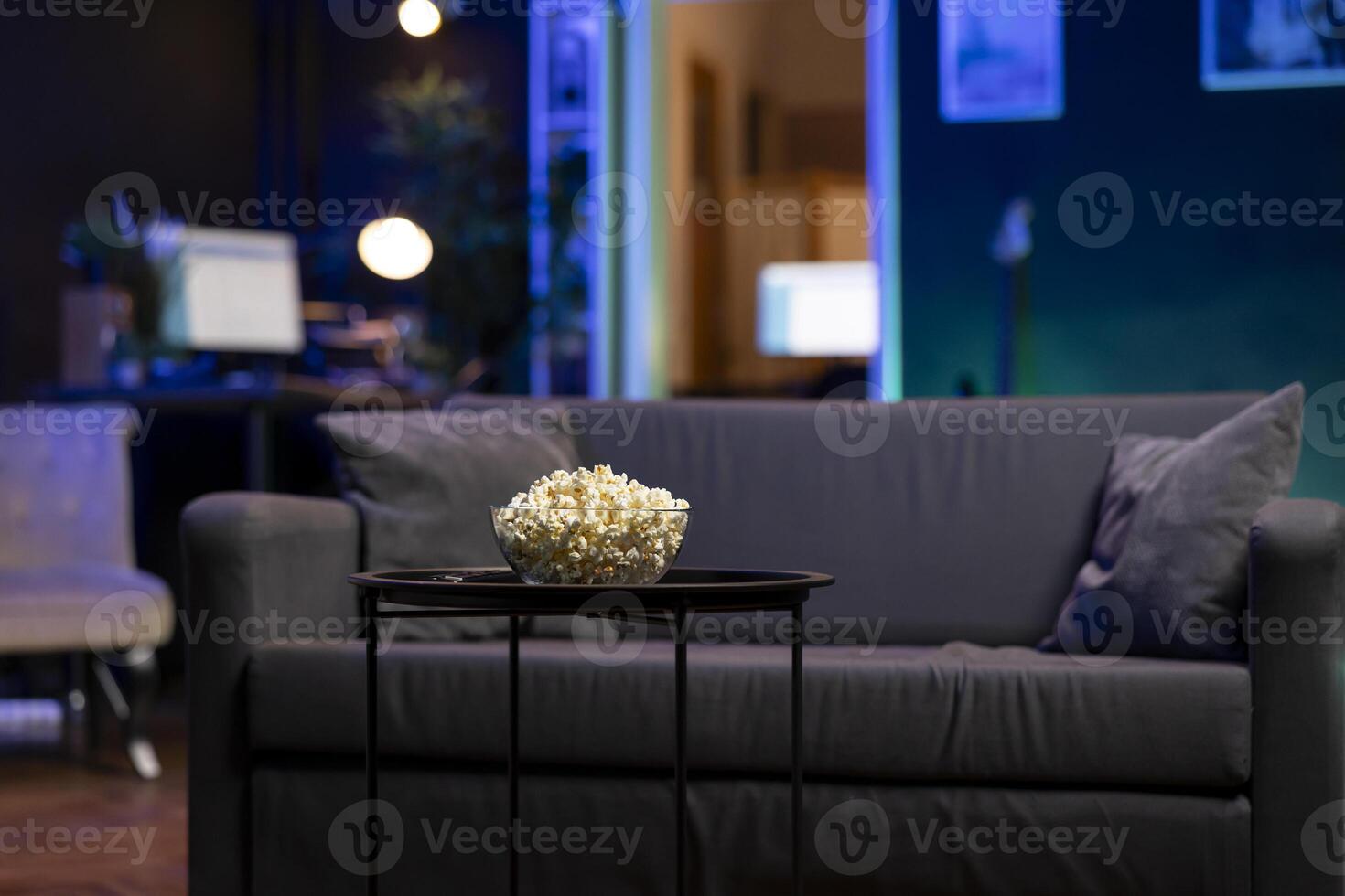 Focus on bowl of popcorn on table with neon illuminated home theater apartment in blurry background. Salty snack prepared for upcoming movie night in cozy RGB lit living room photo