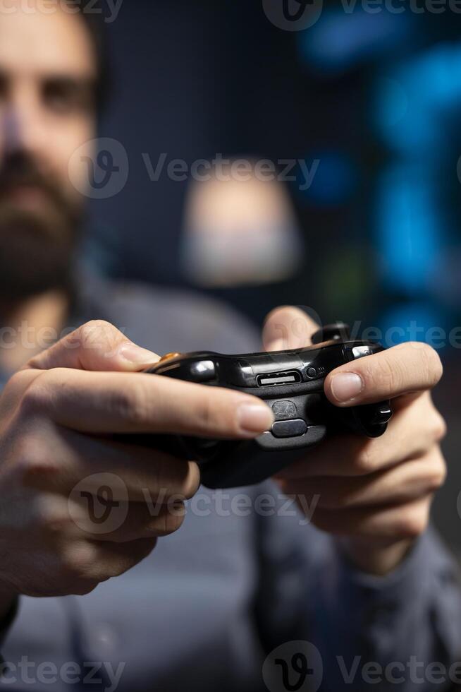 Close up shot of controller held by gamer at home gaming and enjoying leisure time. Focus on gamepad used by man in blurry background in neon lit living room playing videogame on console, relaxing photo
