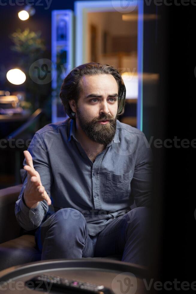 Man watching movies at home on TV, engrossed by riveting action, paying close attention to screen. Man relaxing in apartment on couch, enjoying fascinating film plot and characters photo