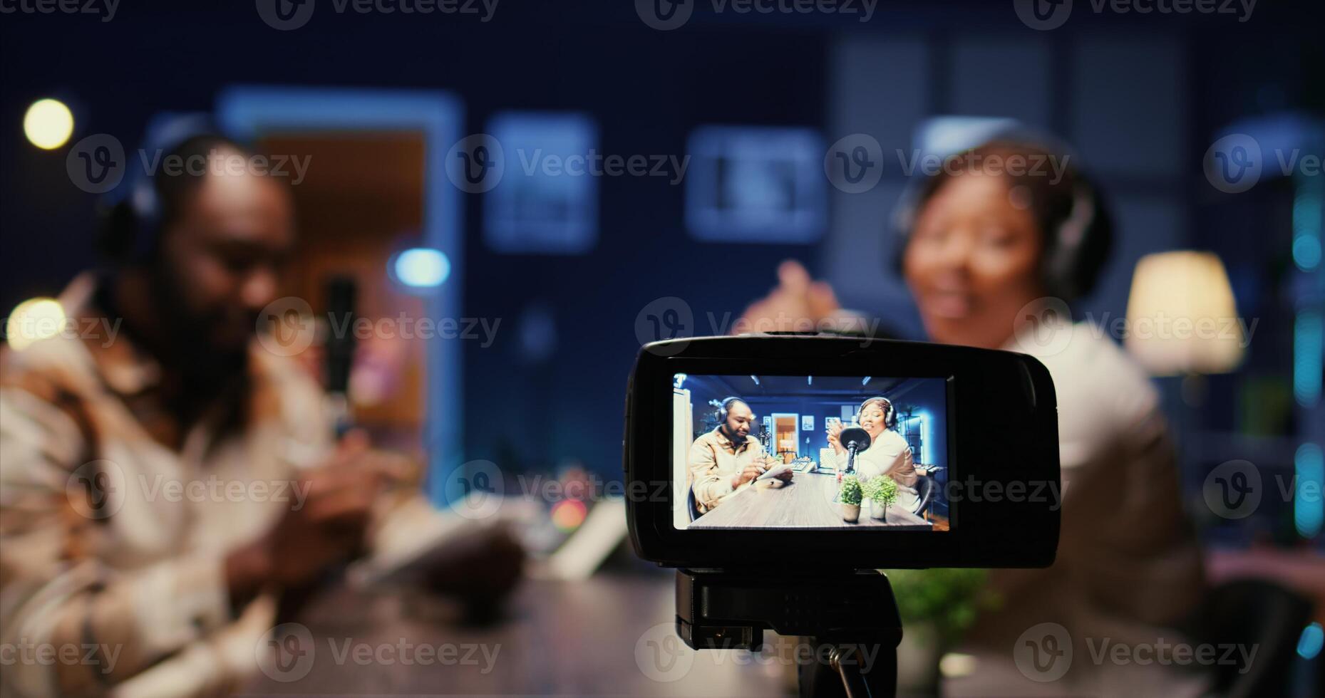 Focus on professional camera recording vlogger show host in blurry background interviewing guest in neon lights studio. Close up shot of equipment used to film online podcast episode photo