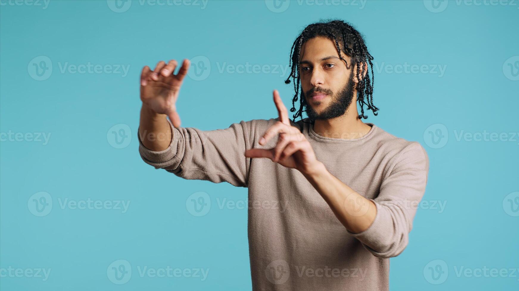 Happy person using augmented reality technology, doing swiping motions. BIPOC man using futuristic AR tech, making pinching zooming gesturing, blue studio background, camera A photo