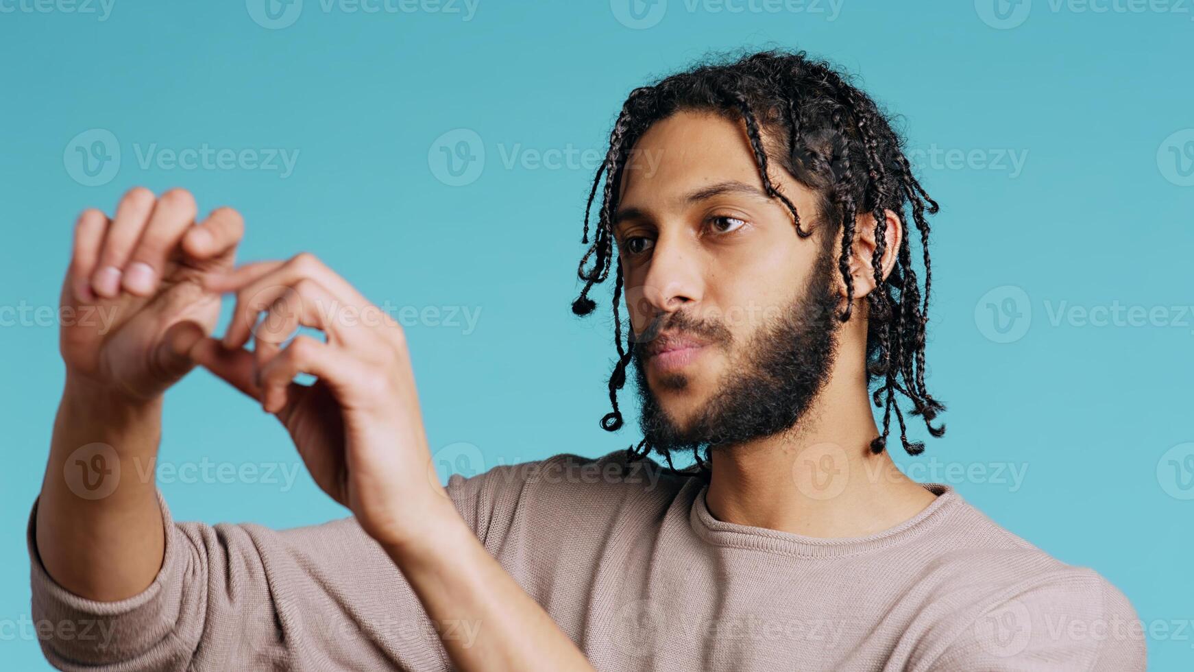 Happy person using augmented reality technology, doing swiping motions. BIPOC man using futuristic AR tech, making pinching zooming gesturing, blue studio background, camera B close up photo