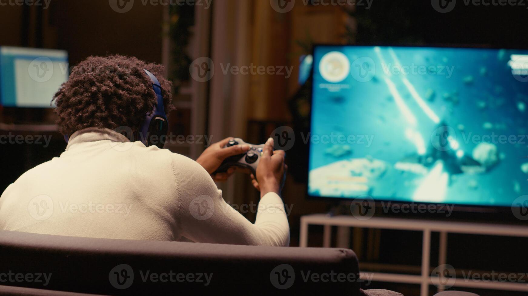 African american gamer excited after winning game playing arcade space shooter on ultrawide TV. Man spending time in apartment on gaming system, happy to finally solve singleplayer videogame mission photo