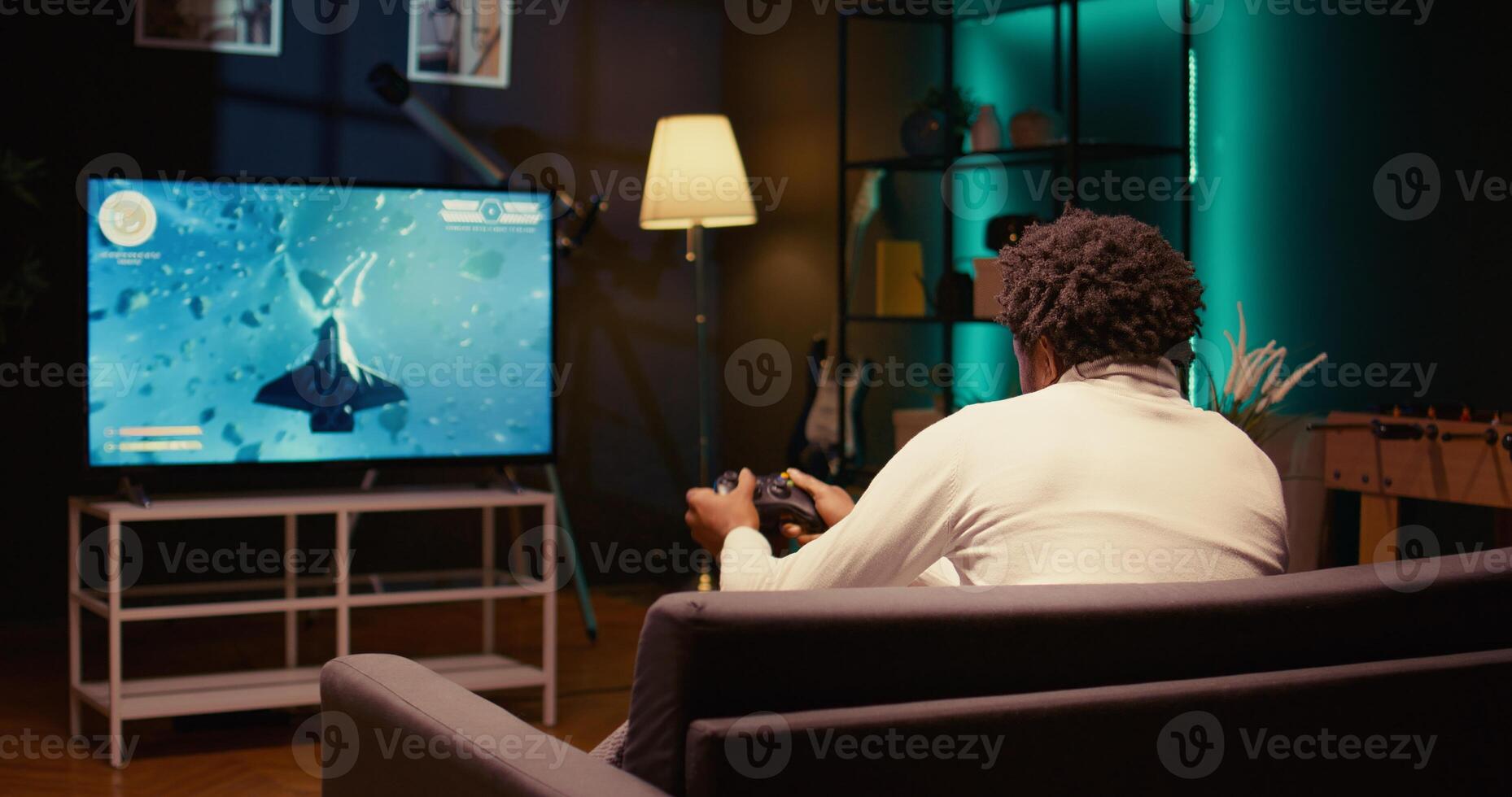 Man plays SF game with overlay HUD showing health bars and minimap on television set. Player enjoying high quality ray tracing graphics in console videogame, zoom out shot photo