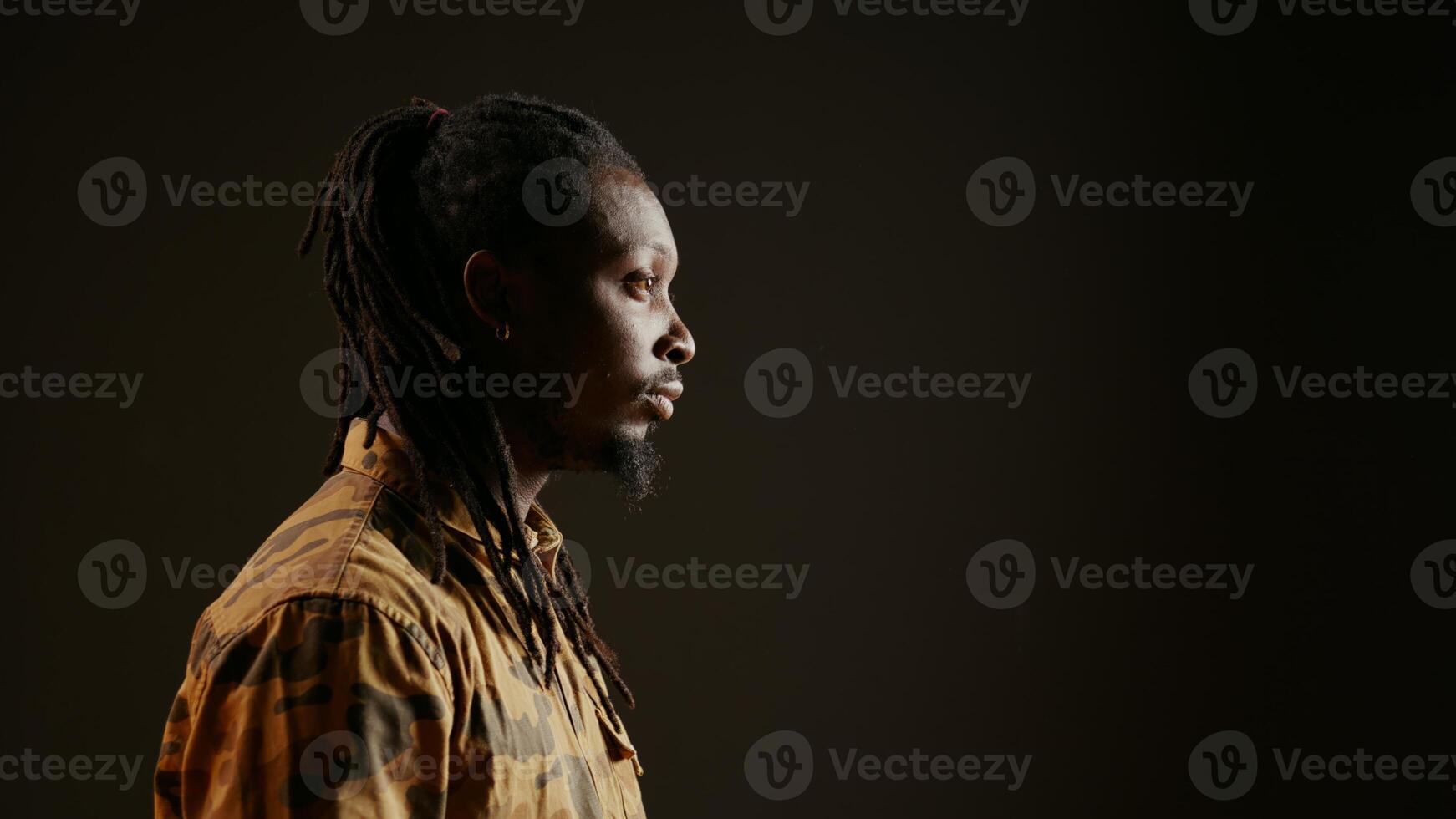 sonriente persona posando en estudio con negro fondo, sensación confidente vistiendo teme y camuflaje ropa. frio chico con de moda pelo interino elegante en cámara, atractivo hombre. Mano disparo. foto