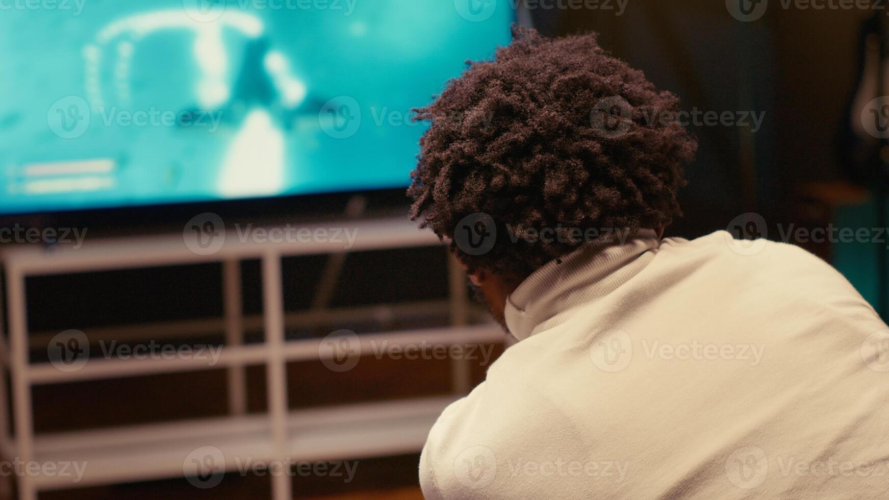 Man in living room using cloud gaming service to play demanding science fiction videogame on TV. Player enjoying high quality ray tracing graphics, streaming game over the internet, close up shot photo