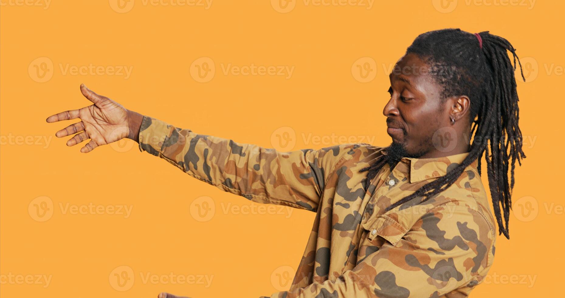 African american guy does advertisement for web marketing, showing thumbs up sign and presenting something to the left. Male model creating ad for promotional campaign. Handheld shot. photo