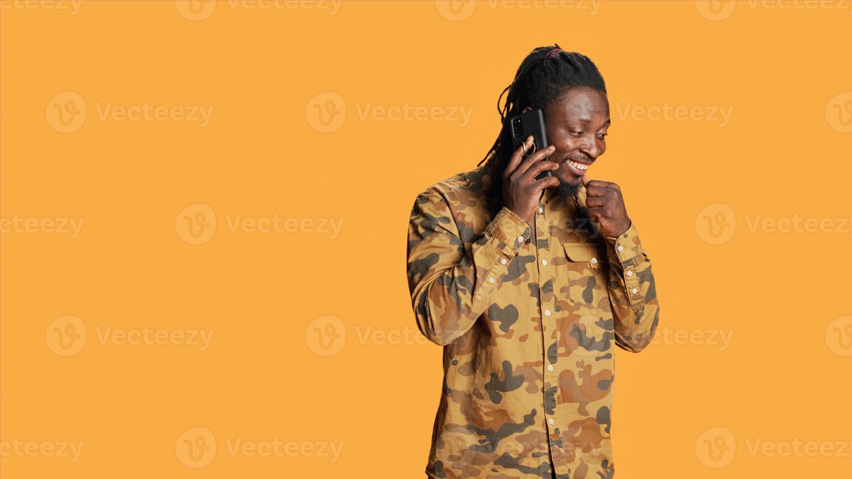Young person answering phone call on camera, talking to friends on remote telephone line over orange background. African american man enjoying telecommunication conversation. photo