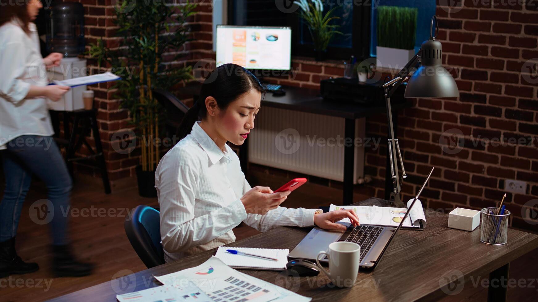 Stressed businesswoman doing multitasking, answering phone while crosschecking data between laptop and paperwork. Worker taking telephone call and comparing financial statistical graphs photo