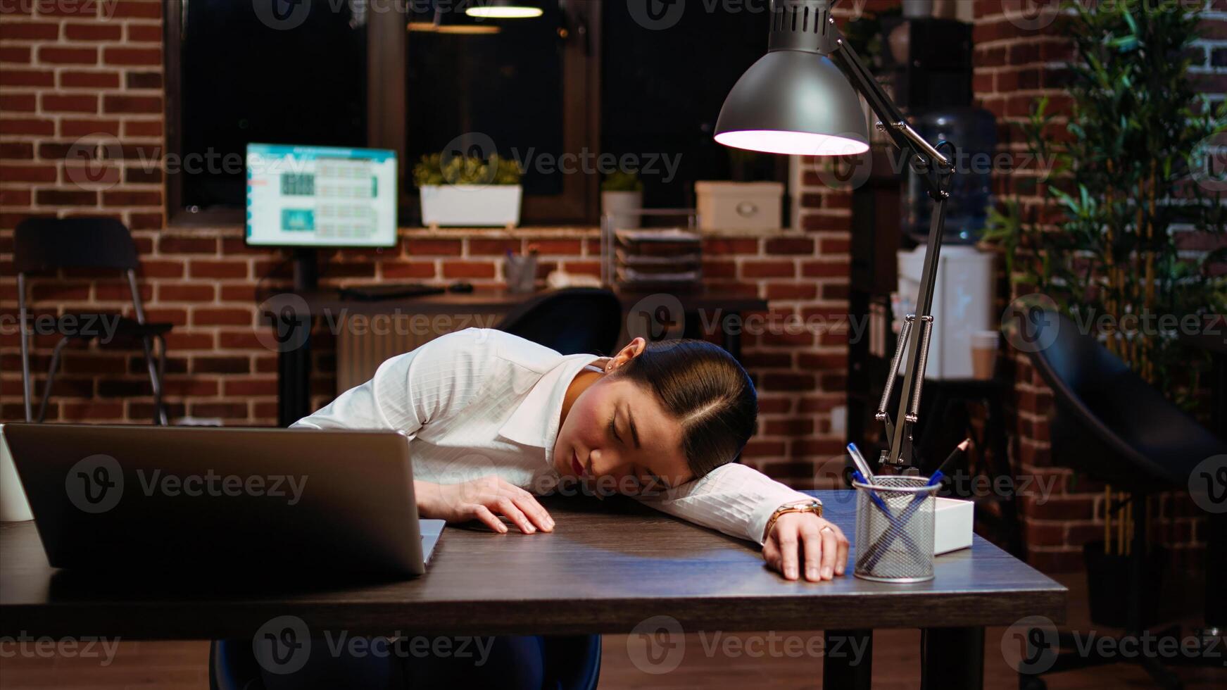 Tired employee sleeping on workspace desk after struggling all night to finish writing emails. Drowsy businesswoman napping in office after working overnight, asleep at laptop, camera A photo