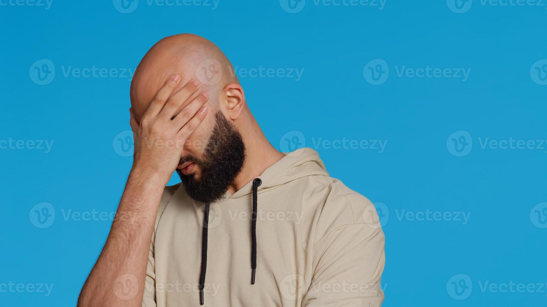 Muslim man suffering from serious migraine on camera, trying to rub temples to ease the pressure. Young middle eastern adult feeling unwell with painful headache, sick person. Camera 2. photo
