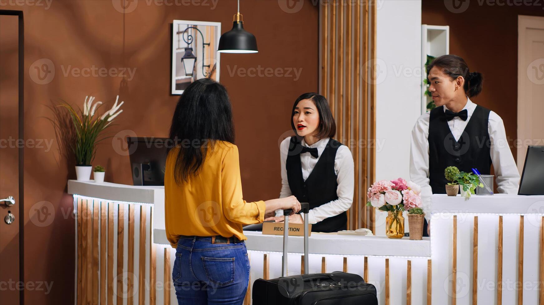 Asian hotel staff greeting customer at front desk entrance, welcoming female client and ensuring pleasant stay during vacation trip. Woman guest arriving in lobby with luggage, tourism concept. photo