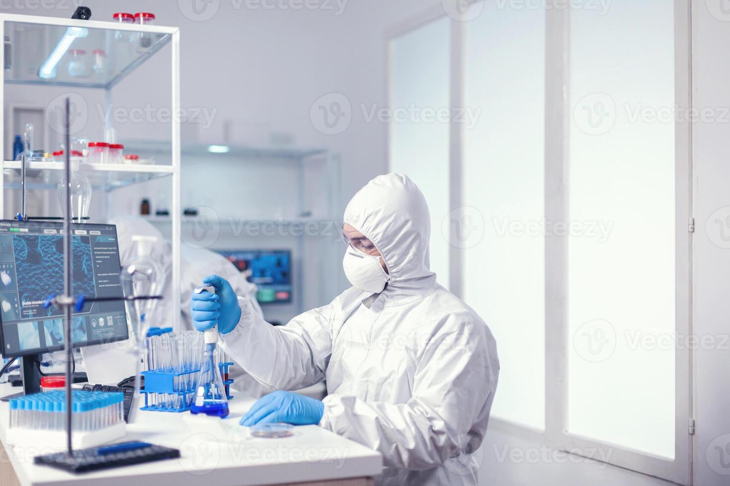 Man scientist filling micropipette with solution from glass flask dressed in coverall. Chemist in modern laboratory doing research using dispenser during global epidemic with covid-19. photo