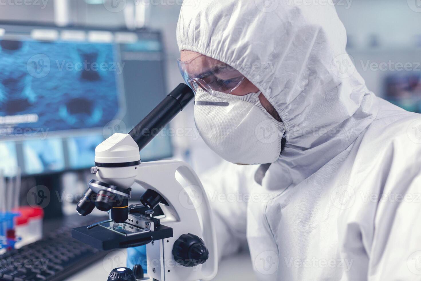 Close up of researcher looking throug microscope in biochemistry laboratory. Virolog in coverall during coronavirus outbreak conducting healthcare scientific analysis. photo