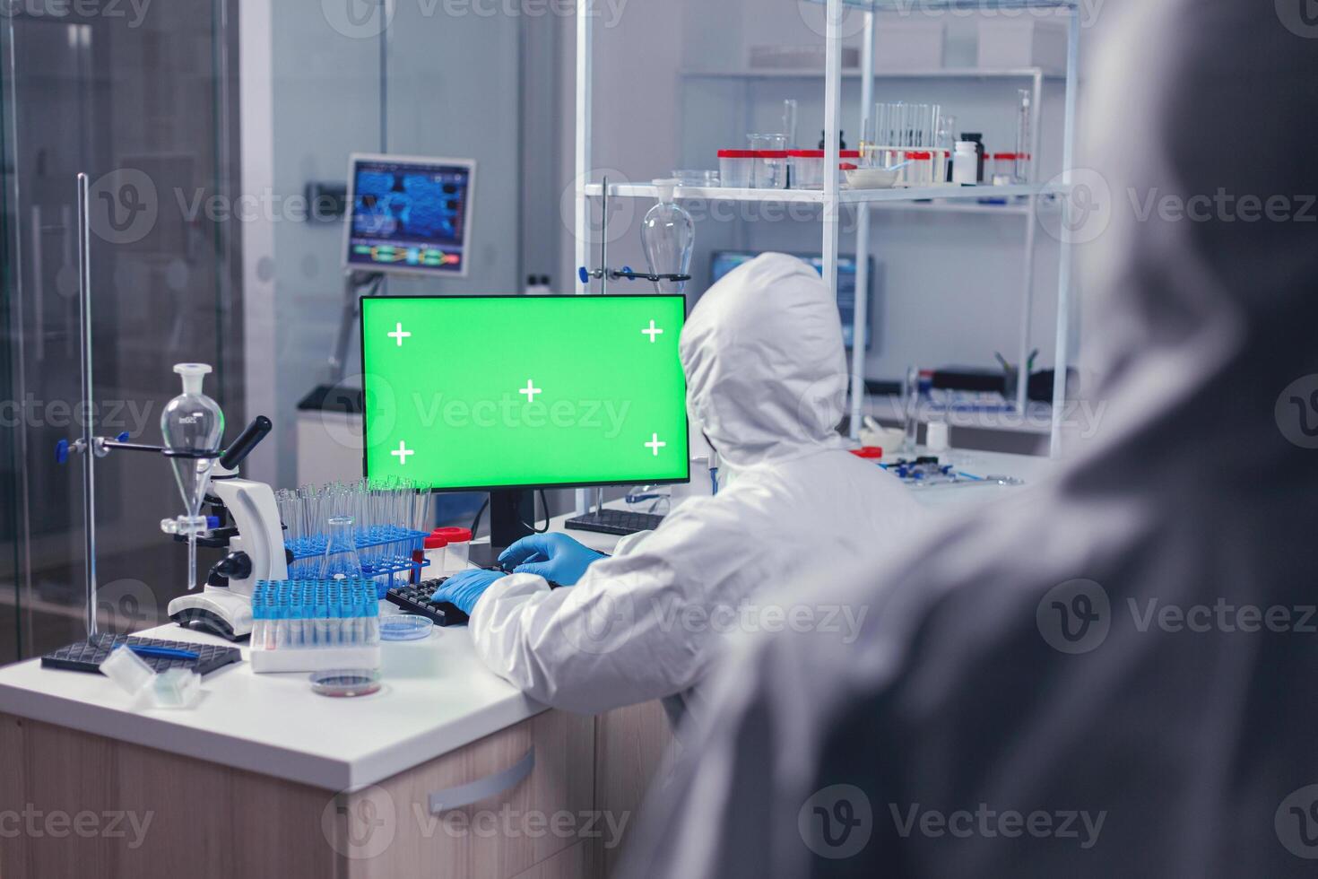 Over shoulder shot of researcher typing on computer with copy space available during coronavirus in laboratory. Team of microbiologists doing vaccine research writing on device with chroma key, isolated, mockup display. photo