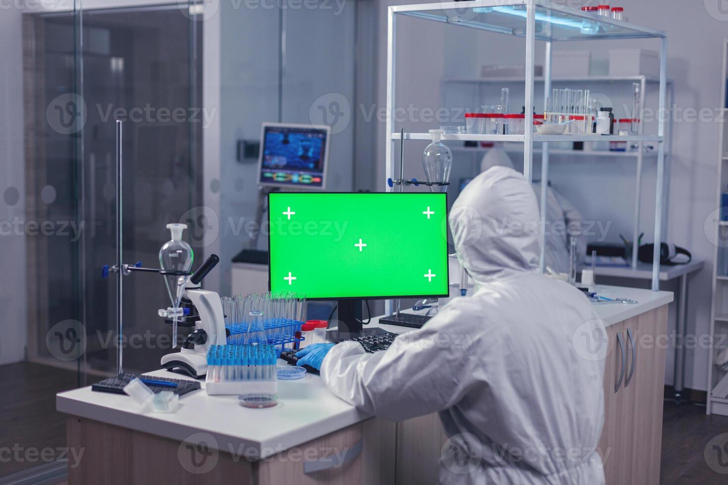 Medical scientist working on computer with green screen sitting at his workplace. Team of microbiologists doing vaccine research writing on device with chroma key, isolated, mockup display. photo