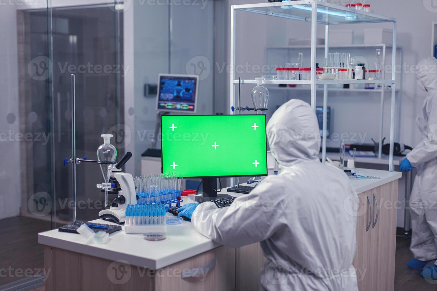 Scientist sitting at his workplace using computer with green screen. Team of microbiologists doing vaccine research writing on device with chroma key, isolated, mockup display. photo