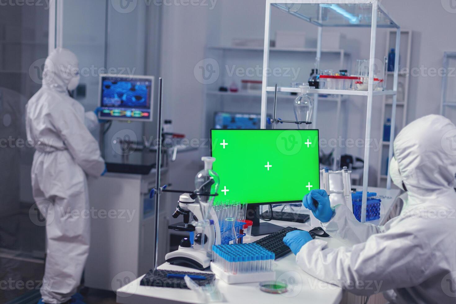 Scientist typing on keyboard works with computer with green screen dressed in ppe. Team of microbiologists doing vaccine research writing on device with chroma key, isolated, mockup display. photo
