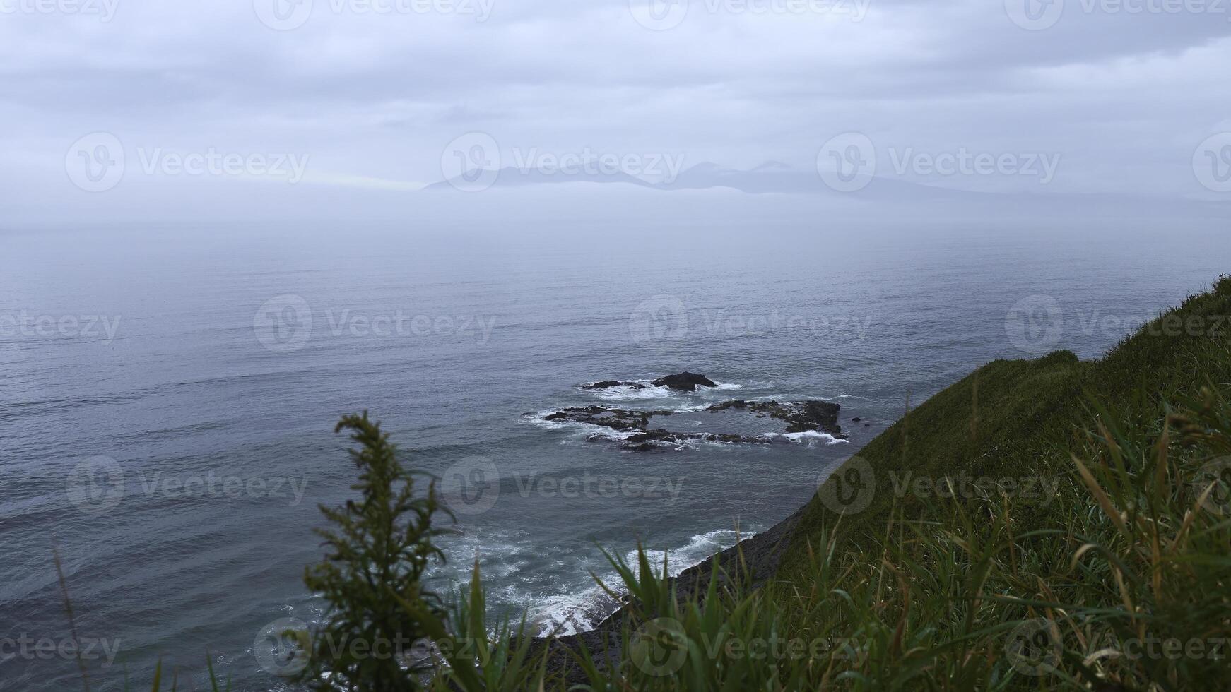 Beautiful landscape from top of green mountain to sea horizon on cloudy day. Clip. Beautiful green grass on mountain ridge of sea coast. Line of mountain coast with green grass and sea horizon on photo