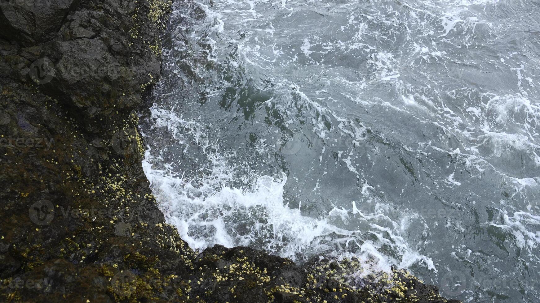 Close-up of surge of waves on rocky shore. Clip. Beautiful waves with splash roll on stones of seashore. Beautiful splashes of waves crashing on rocks on cloudy day photo