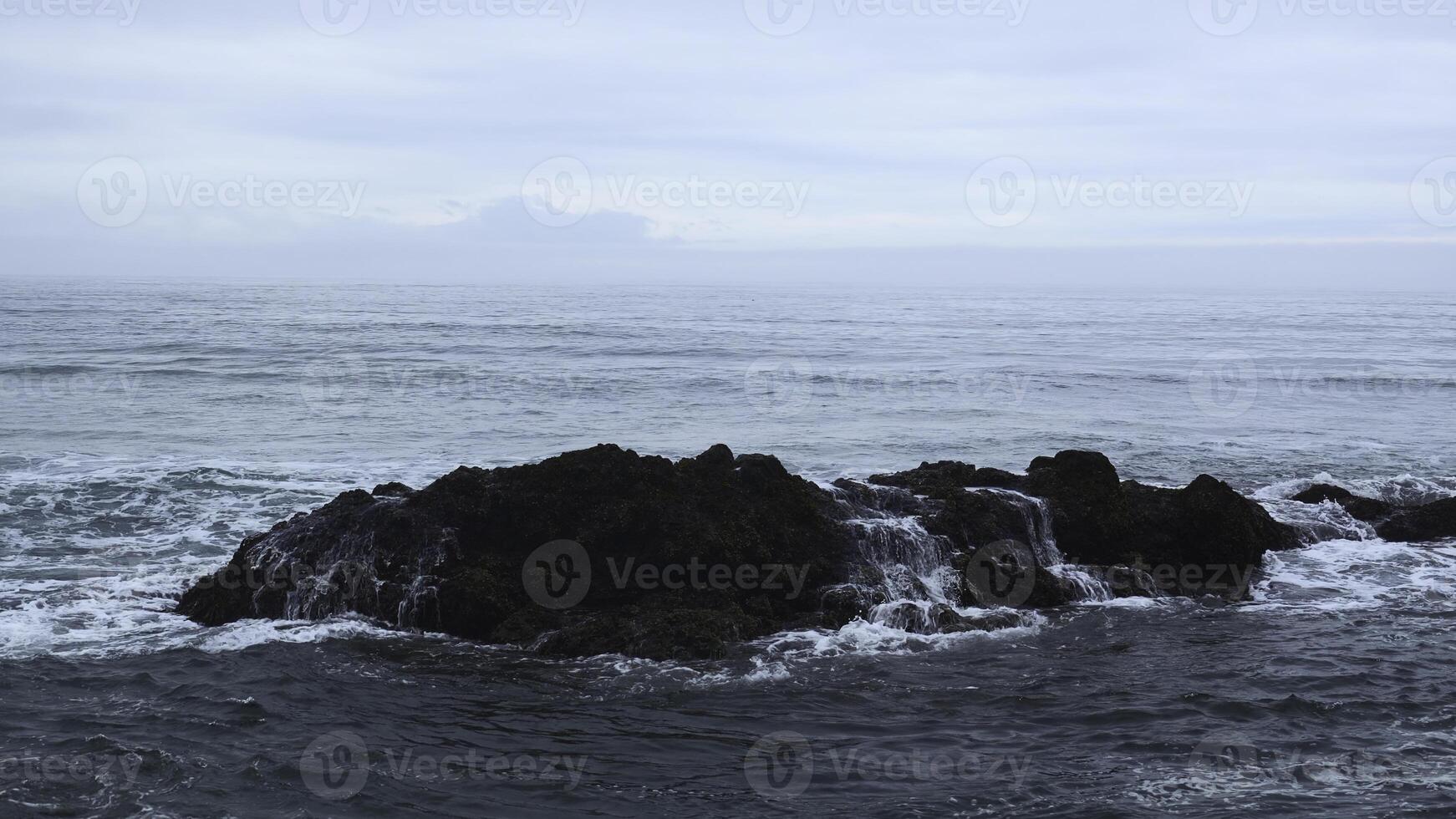 Sea rocks with moving waves on background cloudy horizon. Clip. Rocky rocks stick out in water on seashore on cloudy day. Beautiful seascape with rocks in cloudy weather photo