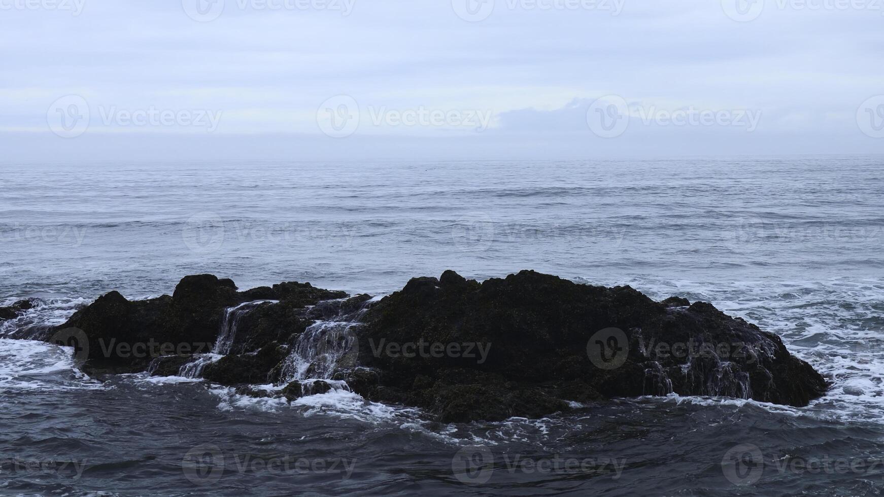 Sea rocks with moving waves on background cloudy horizon. Clip. Rocky rocks stick out in water on seashore on cloudy day. Beautiful seascape with rocks in cloudy weather photo