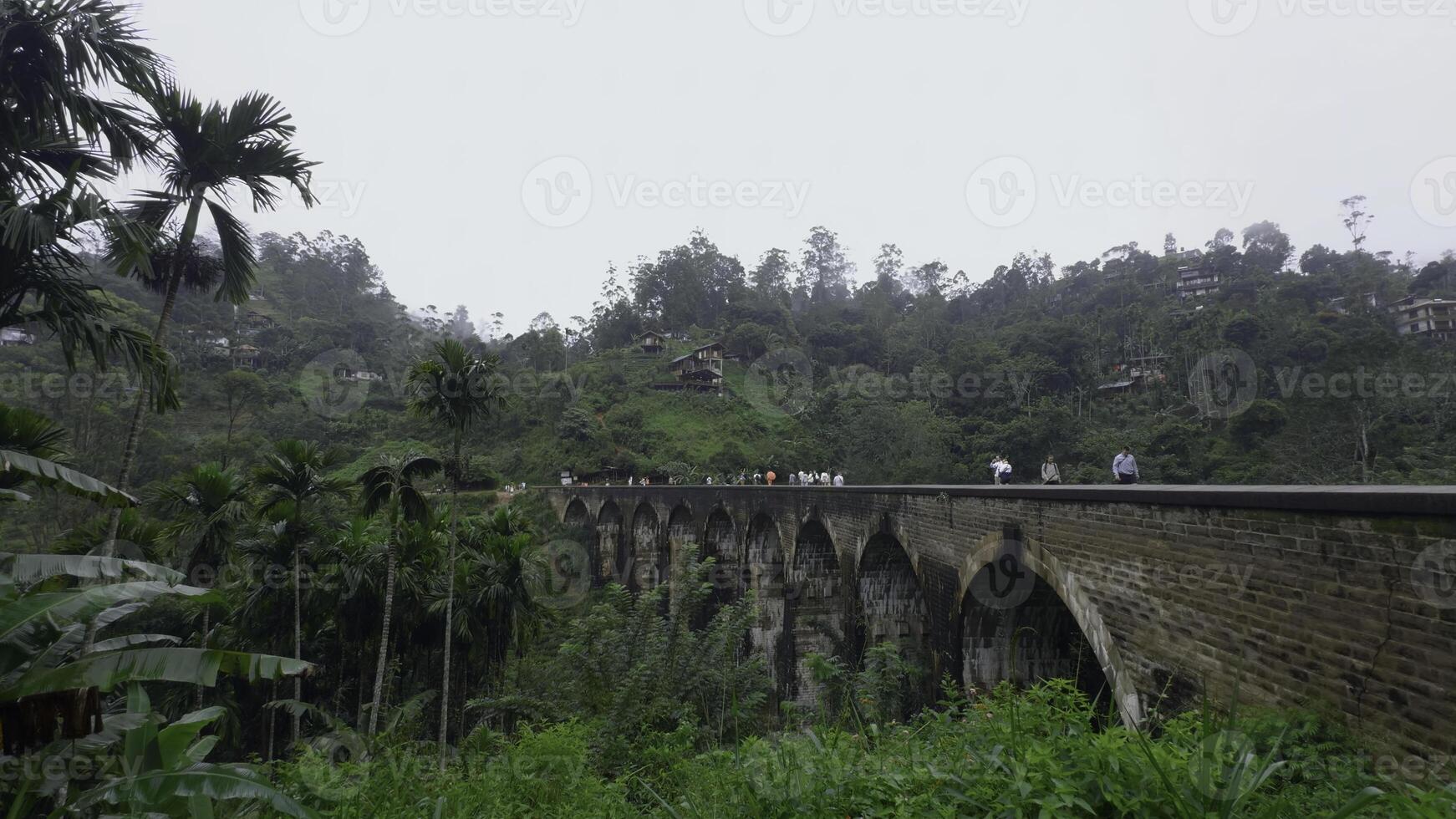 personas caminar en puente en selva montañas. acción. hermosa paisaje con Roca puente en Valle de montaña selva. puente en selva con turistas caminando en nublado día foto