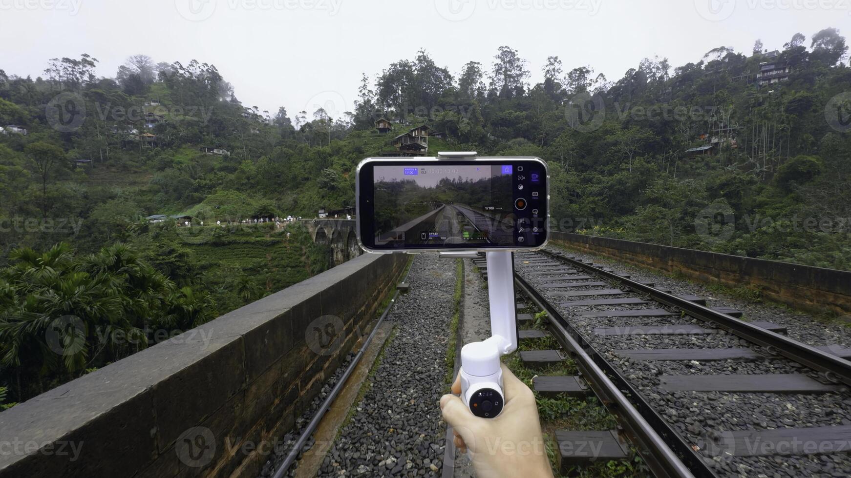 Shooting on tripod phone while traveling. Action. Shooting video on phone with stabilizer while traveling. Shooting bridge with railway in jungle on phone for blog photo