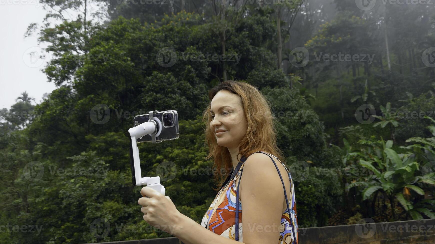 Beautiful woman takes pictures on phone with tripod. Action. Woman professionally shoots landscapes on phone while traveling for blog. Shooting for travel blog photo