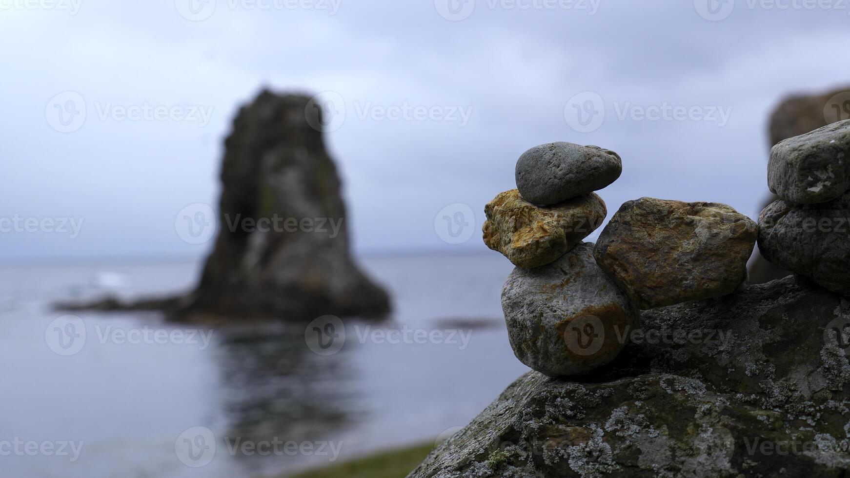 Close-up of stacked rocks on beach with rocks. Clip. Stones stacked in composition on blurred background of rocks in sea. Stones stacked in turret stand on background of overcast sea photo