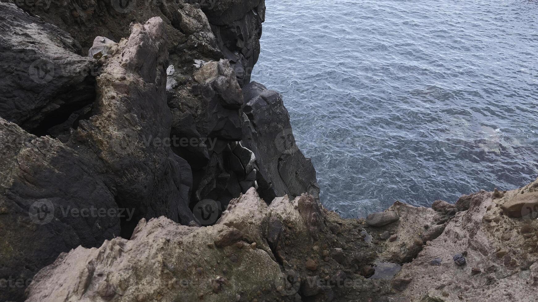 Beautiful rocks by water. Clip. Stone cliffs of coast with quiet sea water. View from edge of stone shore to sea water photo