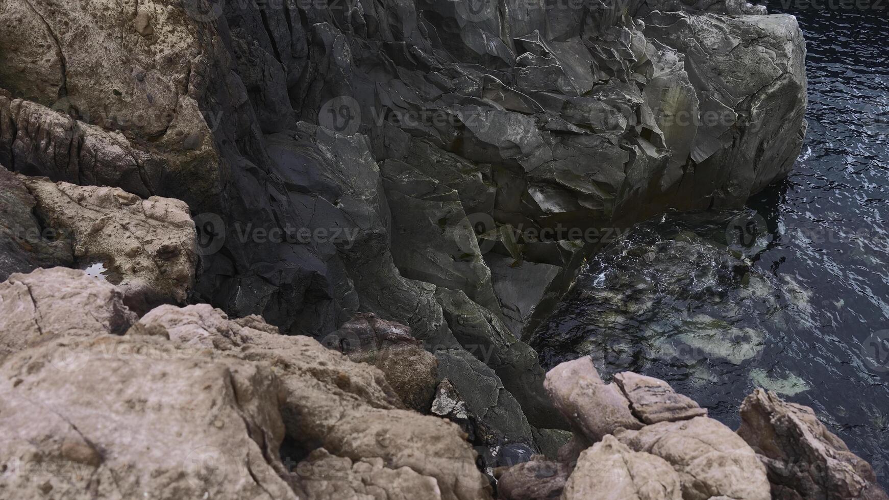 View of dangerous stone cliffs near sea water. Clip. On edge of dizzying cliffs by sea water. Beautiful and dangerous sharp rocks with sea water photo