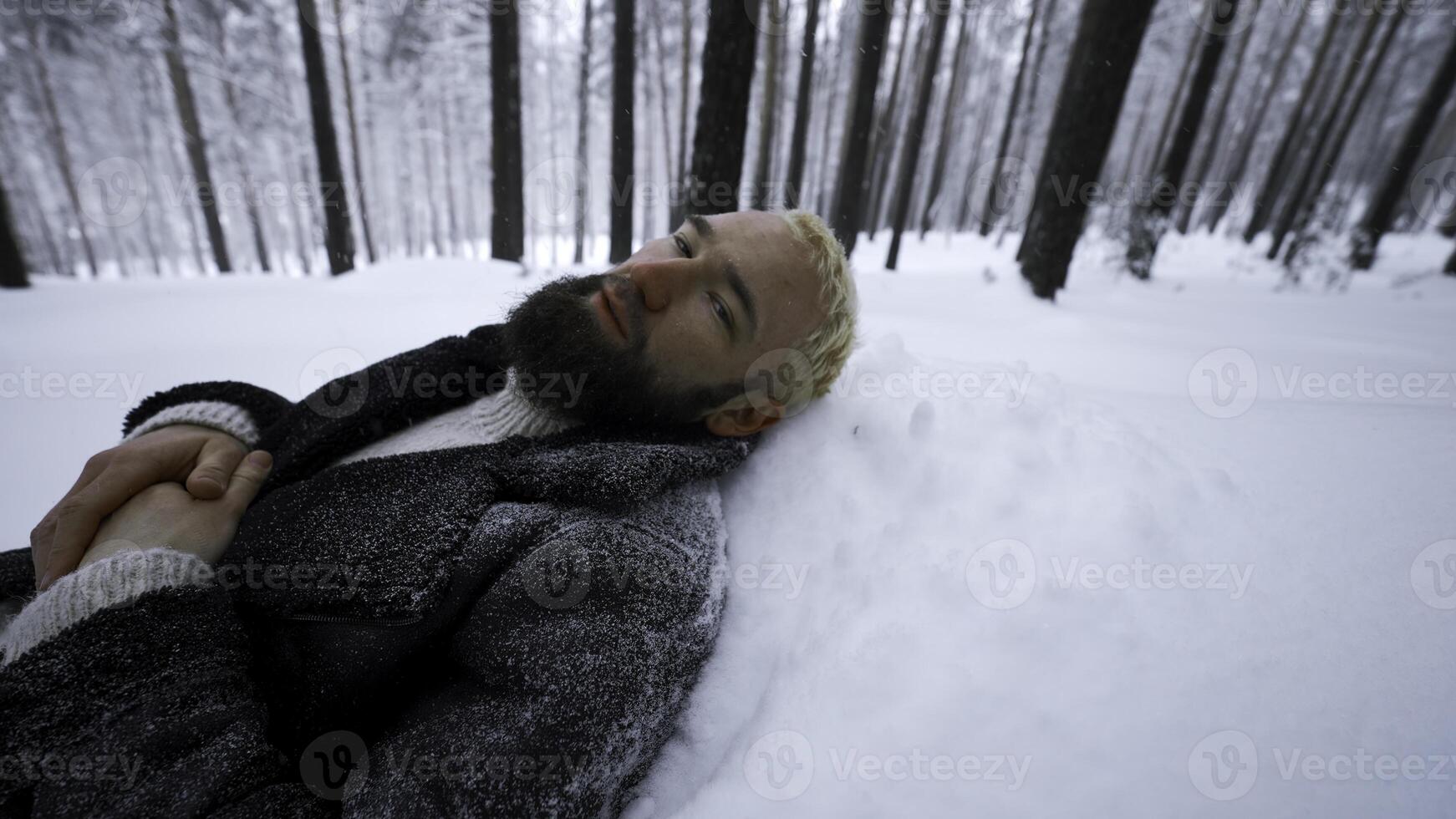 Man lies in snow in winter forest. Media. Tired man lies in snowdrift in winter forest. Depressive Stylish man lies in snow in winter forest photo