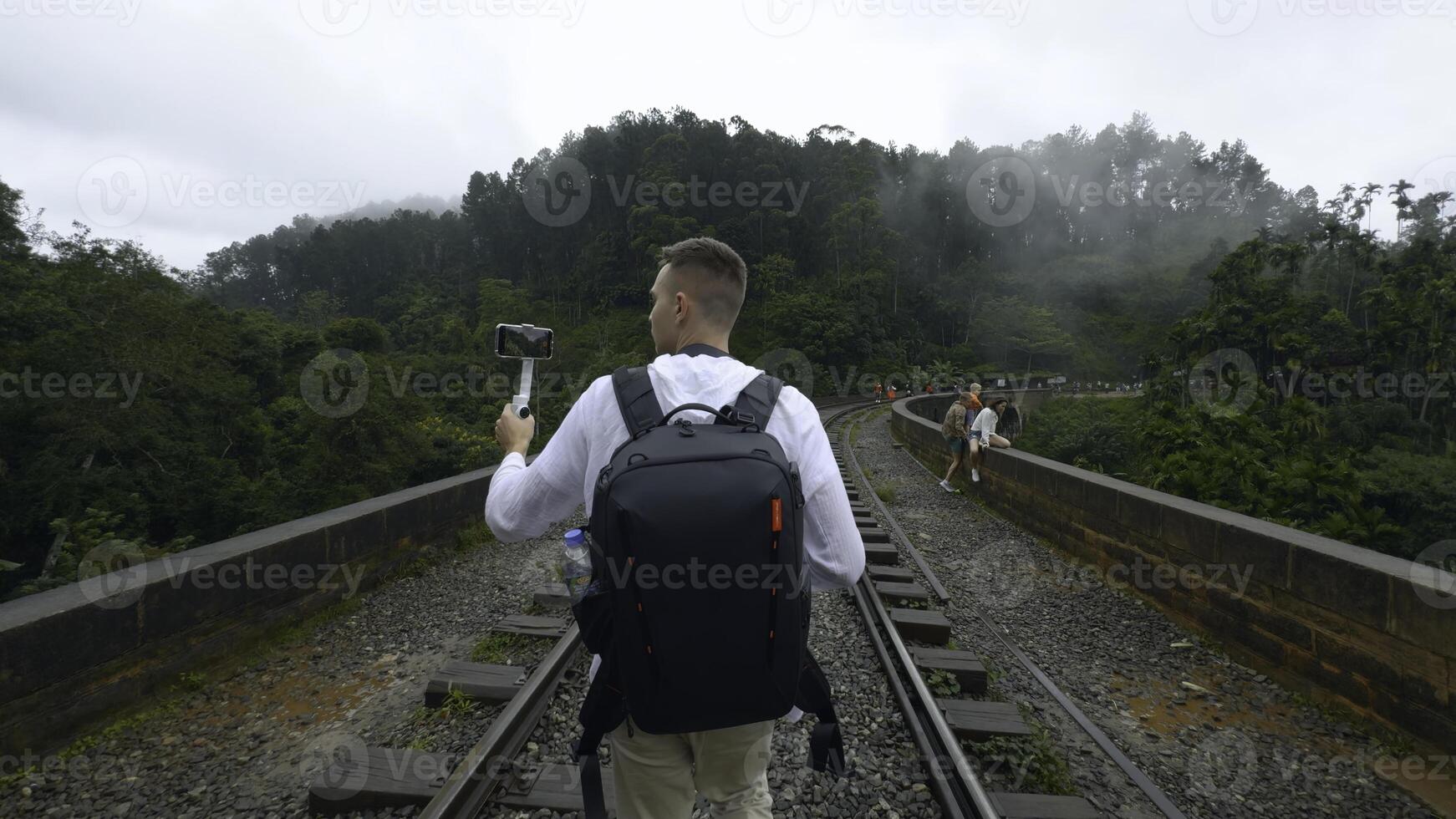 Man on hiking trip on tropical bridge. Action. Man on hiking trail with stone bridge and railway. Man walks on stone bridge in tropical mountains photo