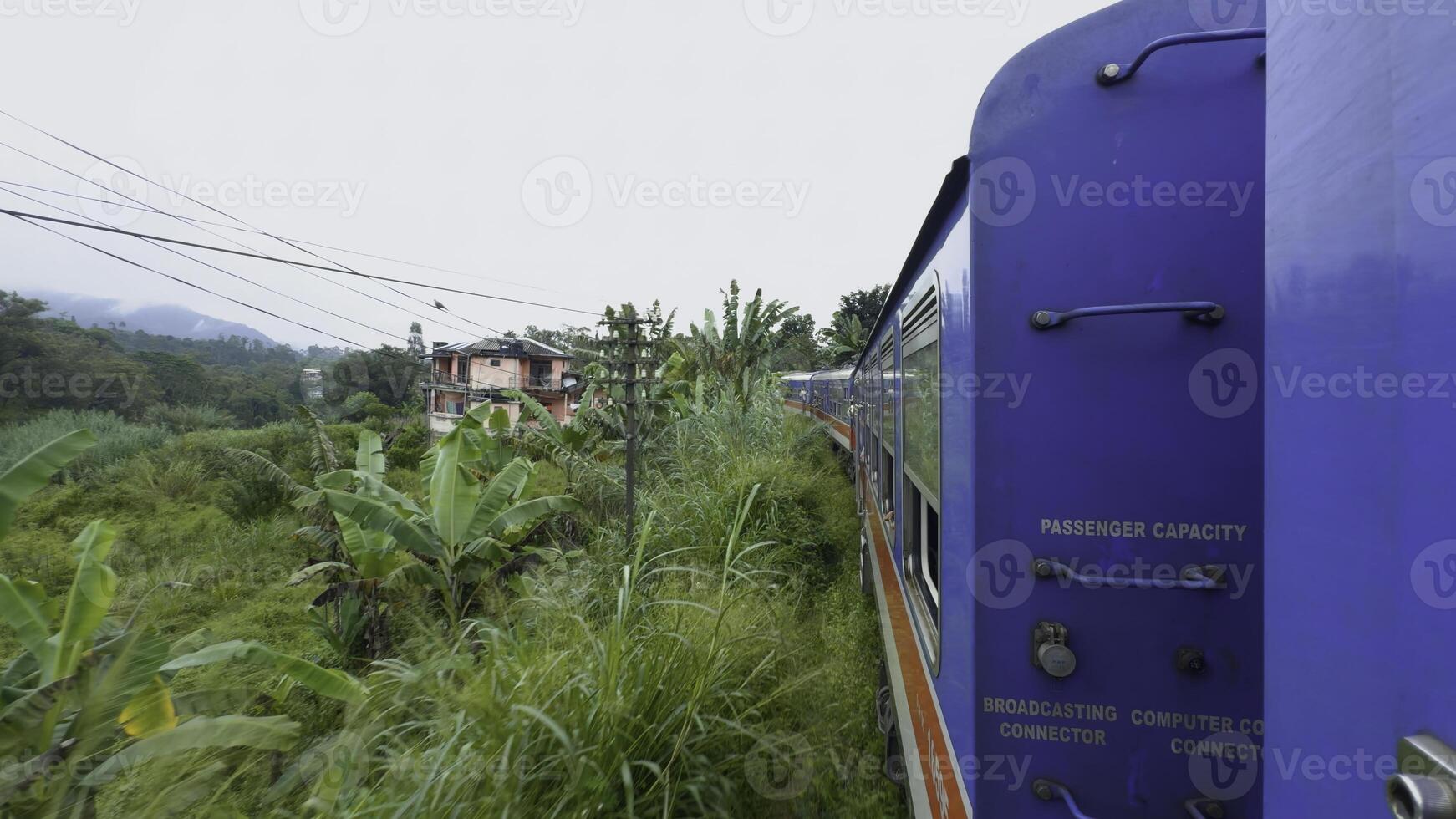 View from window of moving train in jungle. Action. Traveling train in midst of green forest in tropical mountains. Beautiful train ride in tropics on cloudy day photo