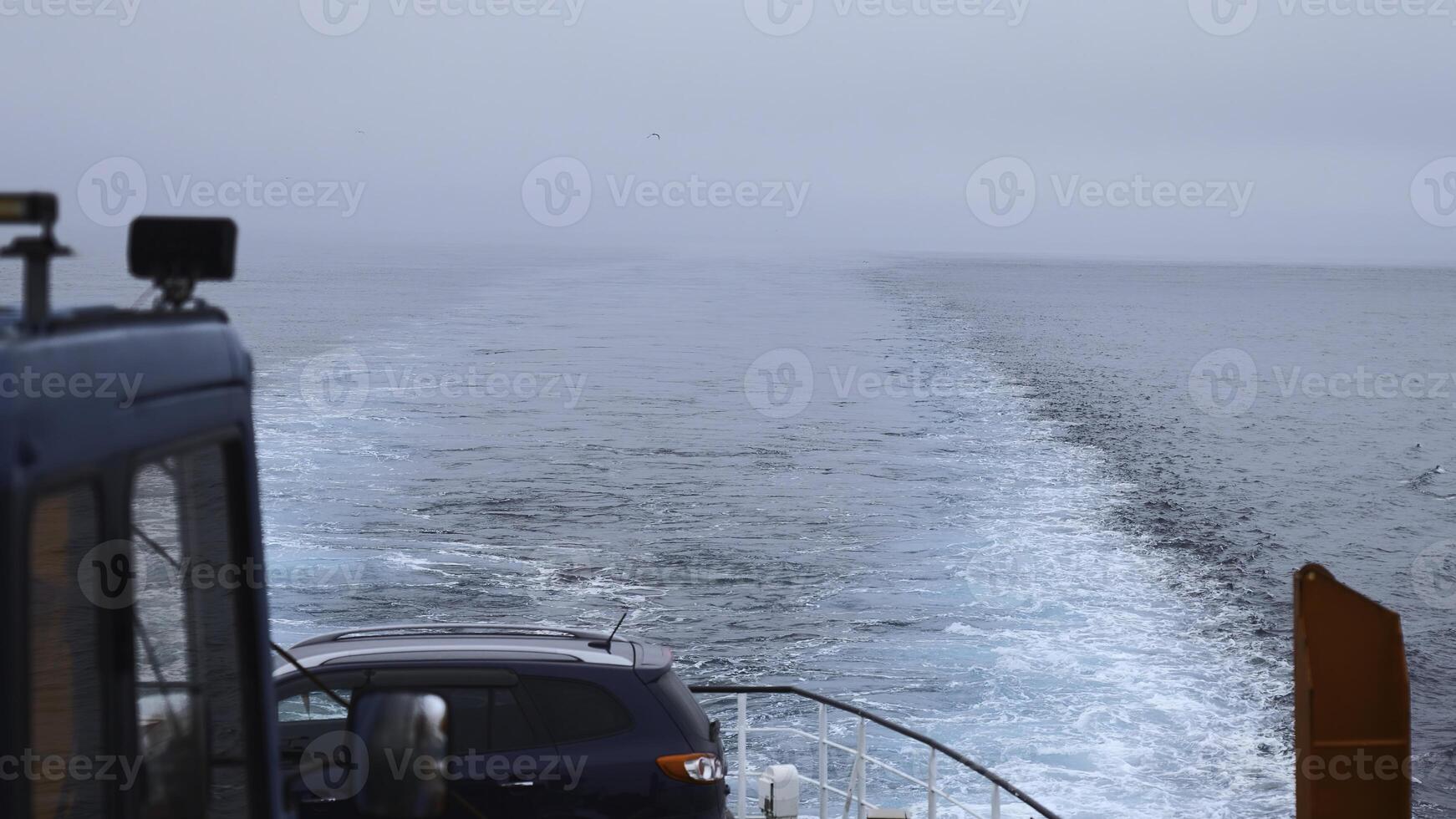 Ship with car sails into sea in cloudy weather. Clip. Sailing on ferry with car in sea. View of line left by sailing ship at sea on cloudy day photo