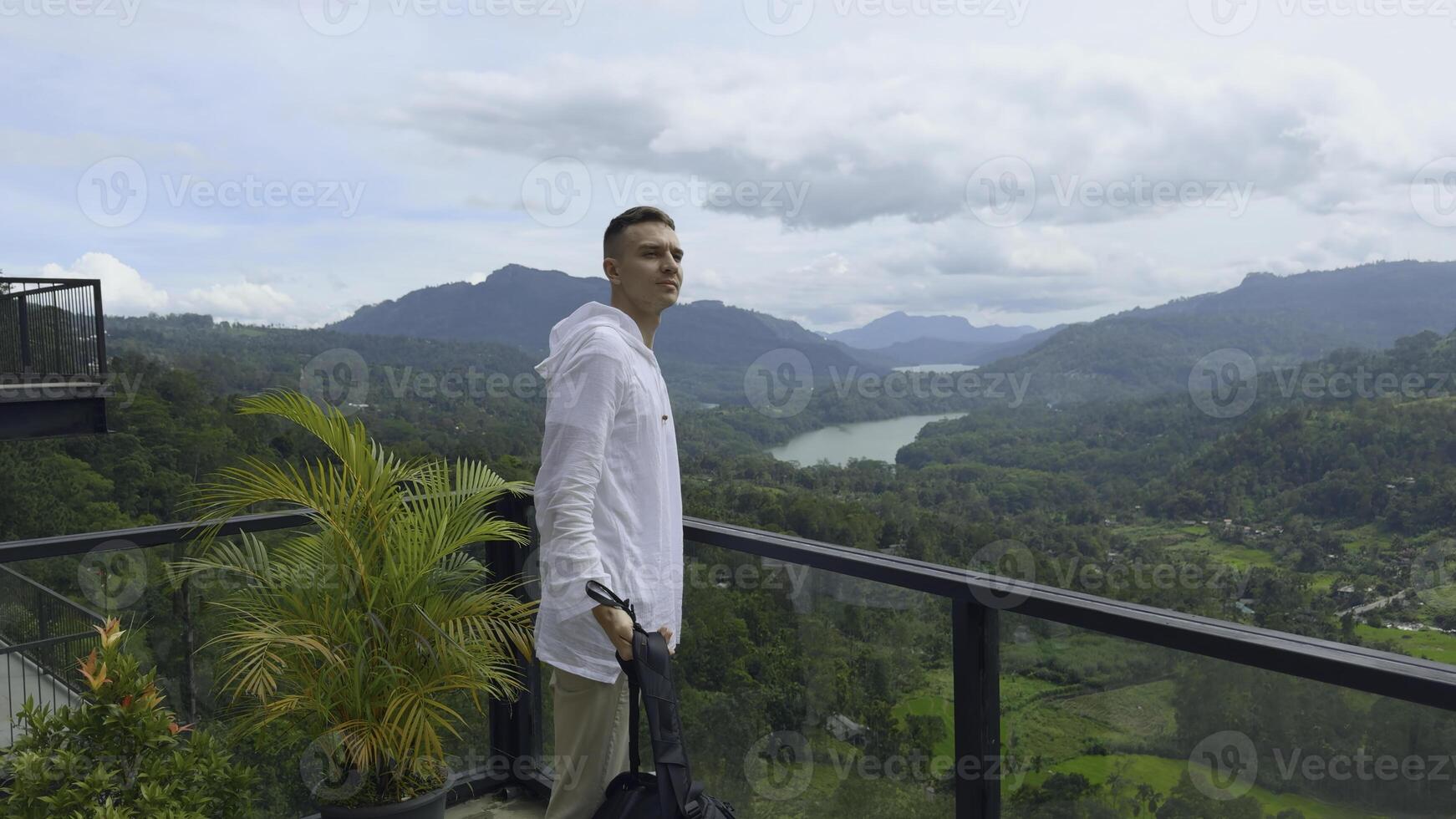 Man with view of tropical mountain valley. Action. Man on observation deck in tropical mountains. Man with backpack on sightseeing attraction overlooking green mountains photo