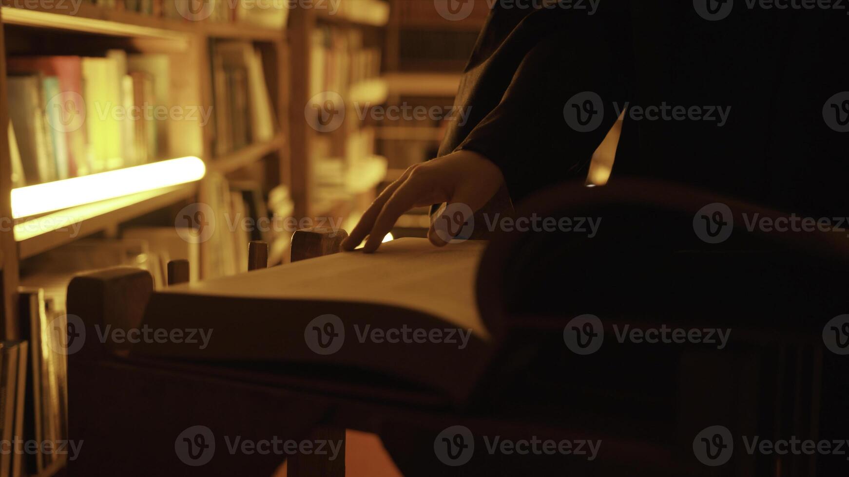 Close-up of mysterious man opening large book. Stock footage. Man opens book in dark library with flashing light. Secret society with mysterious books in night library photo