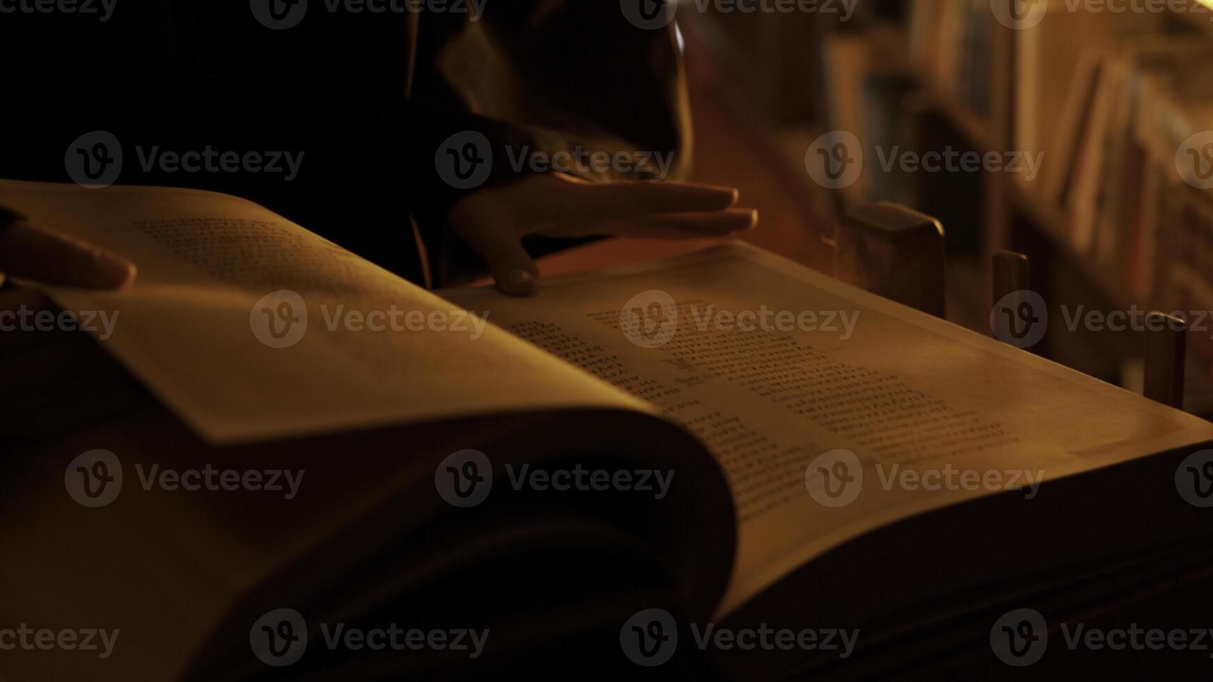 Man reading large mysterious book. Stock footage. Close-up of mysterious man reading ancient forbidden book in library. Secret society with books in night library photo