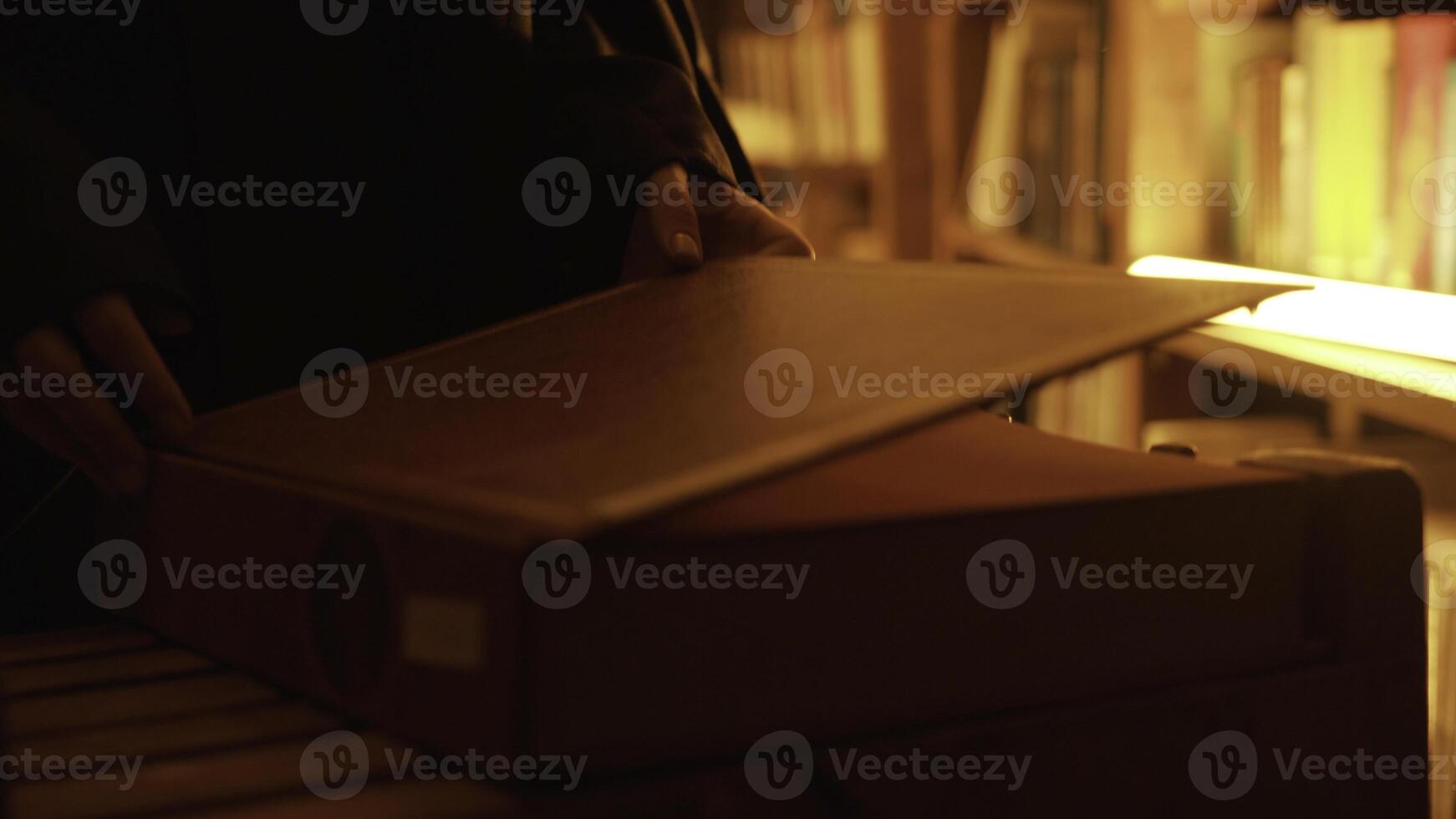 Close-up of mysterious man opening large book. Stock footage. Man opens book in dark library with flashing light. Secret society with mysterious books in night library photo