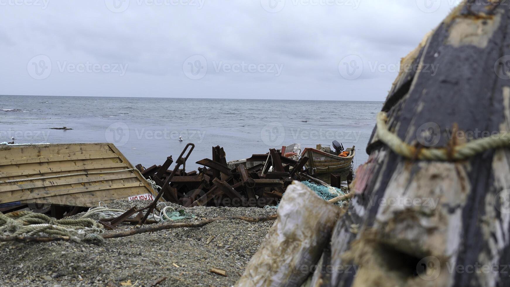 Ruins of fishing boats and garbage on seashore. Clip. Garbage and ruins of sea boats on shore on cloudy day. Debris and destroyed boats after storm on seashore photo