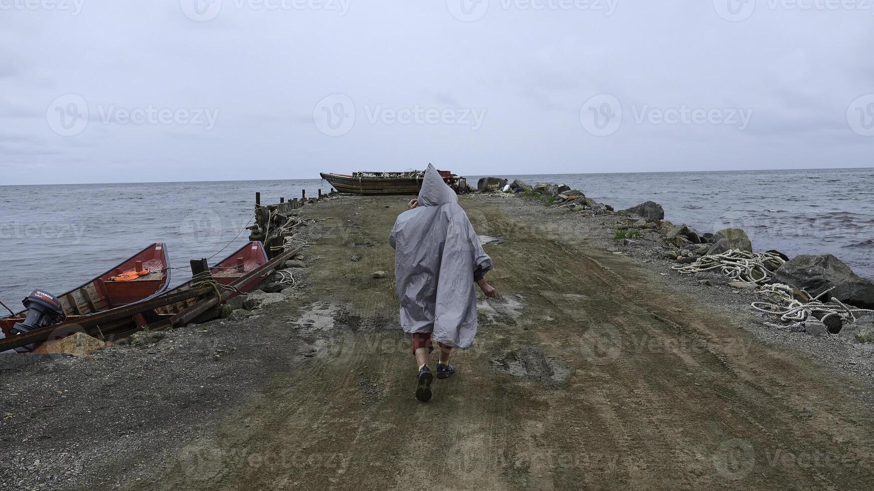 Man walks along pier to fishing boat. Clip. Man on stone pier goes to fishing boat. Man walks along embankment with fishing boats on cloudy day photo